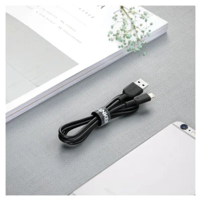 Complete coiled Black Anker PowerLine II USB-A to Lightning cable on a desk beside a book and phone